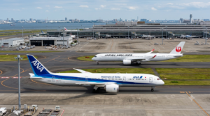 羽田空港の誘導路をタキシングする、全日本空輸（ANA）のボーイング787と、日本航空（JAL）のエアバスA350-1000。背後にターミナルビルが見える。