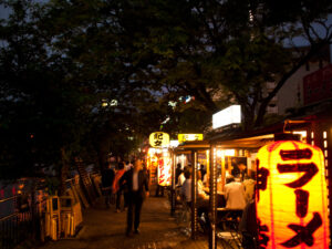A night view of the Nakasu food stall district in Hakata, with the glow of ramen stalls and paper lanterns spreading along the riverside.